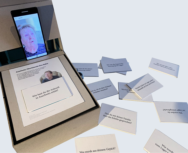 A smartphone plays an interview with Auschwitz survivor Else Baker while printed interview cards with student questions are placed around the board.